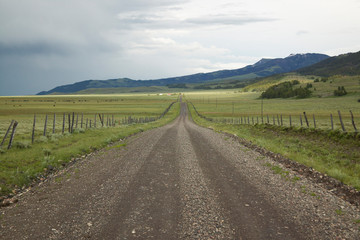 Fototapeta na wymiar Dirt road into Centennial Valley, Montana with incoming storm, green fields and mountains