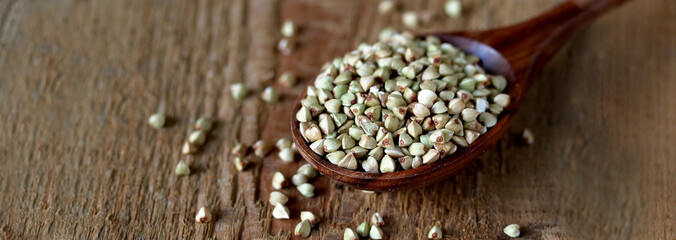 green buckwheat in a wooden spoon on a wooden background. rustic style organic. super food. healthy groats