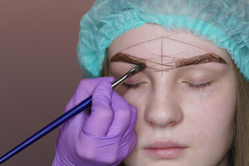 Young woman undergoing eyebrow correction procedure in beauty salon, close up. Beauty treatment at spa salon. Beautician paints eyebrows. .