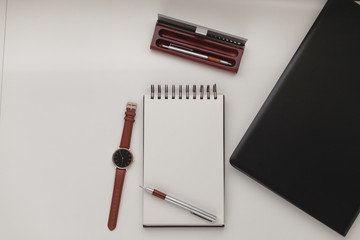 Minimalist workspace background with laptop, pen, pen case, wrist watch and open notebook. White office desk frame