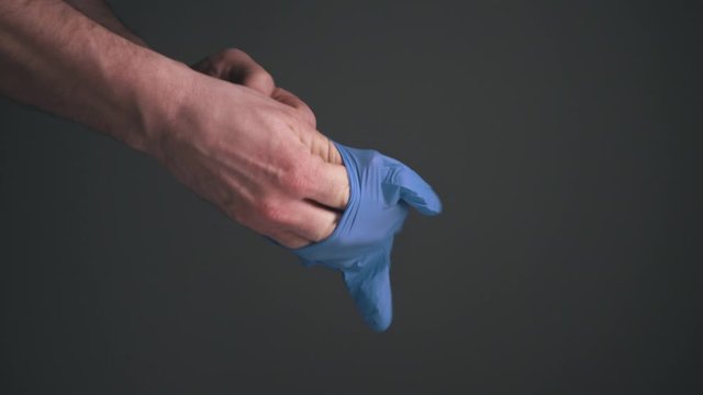 Cinematic dark background, adult caucasian male hands, carefully put on blue plastic nitrile medical gloves in calm minimalistic scene ready to add text.