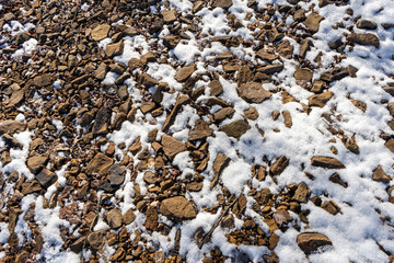 Rough, red, craggy rocks are covered with a dusting of snow on a lake shore in western Maryland, United States.