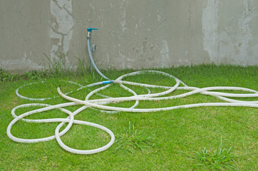Long white rubber band for on green lawn wit faucet on concrete wall
