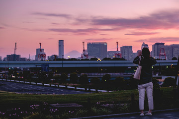 Fototapeta na wymiar Woman taking photo of Tokyo skyline at sunset with her mobile