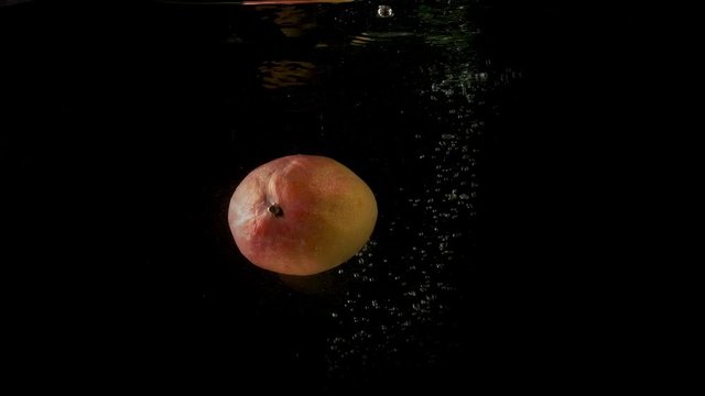 Sweet delicious mango falling in the dark and clear water. Steady underwater slow motion camera shot.