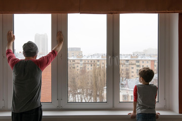 Quarantine. Isolated father and his son looking through the window. Moscow, Russia.