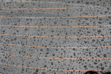 Drops of water on the rear window of the car, orange heating threads. Black tinted car glass with a heating element wet in the rain