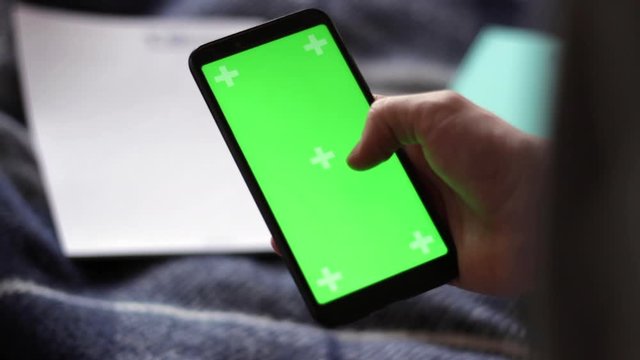 Hand holding smartphone with blurred paper and pen, green screen