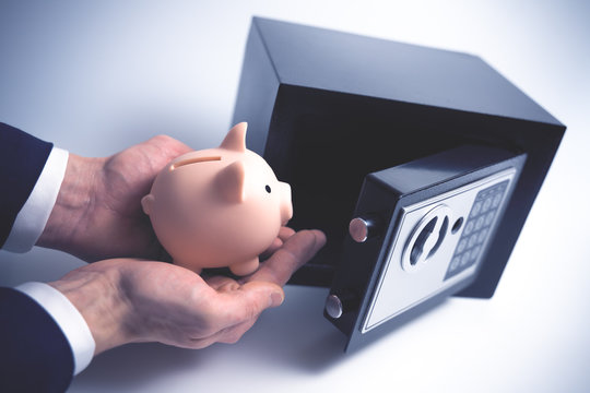 Cash Money Safe Deposit. Symbol of savings safety. The man puts a Piggy bank in small Residential Vault. Toned soft focus picture.