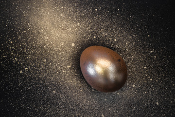 Golden egg and paint splashes on black background. Abstract cosmos. Happy easter minimal concept