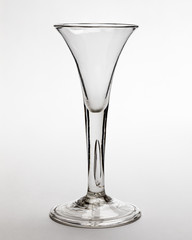 An 18th century antique tall clear wine glass on a light background.