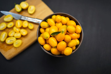 Kumquat in a bowl and on a wooden board cut into slices on a black background