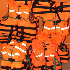 A many orange bright marine life vest in stack close up, safety on water tourism activity, yachting and watersports