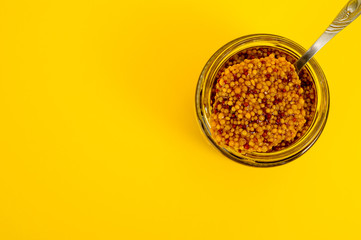 French mustard in a glass jar, shot on a yellow background. Background for seasoning and nutrition.