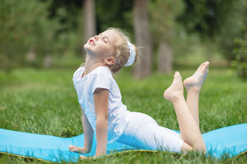 Portrait of little child girl doing yoga in in green grass