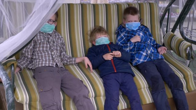 Three funny boys swing on swing in a supermarket. Children put on protective medical masks because of coronavirus epidemic