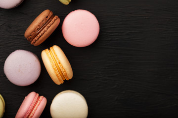 Macaroni cookies of different colors lie on a black textured background. Free space. Still life of confectionery.