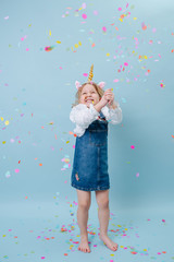 Smiling little girl in unicorn head band catching confetti from air over blue