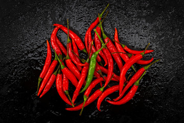 One green chili pepper on red chili peppers on black table