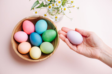 Woman hand holding a painted easter egg next to a full bowl of them
