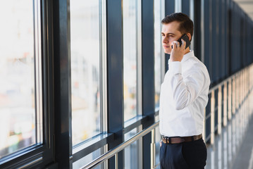 Portrait of a serious confident man boss having mobile phone conversation while resting after meeting with his partners, businessman talking on cell telephone while standing in modern space indoors