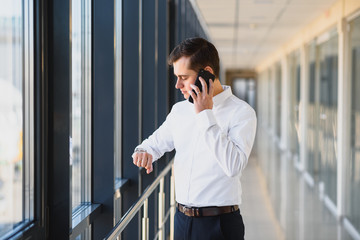 Portrait of a serious confident man boss having mobile phone conversation while resting after meeting with his partners, businessman talking on cell telephone while standing in modern space indoors