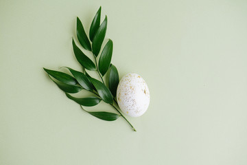 Gilded easter egg and plant branch on a green surface. Top view
