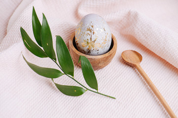 Easter egg in a stand, spoon and plant branch on a pink tablecloth