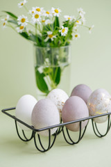 Gilded easter eggs on a metal egg holder next to glass with chamomiles