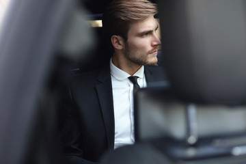 Confident businessman in full suit sitting in the luxe car.