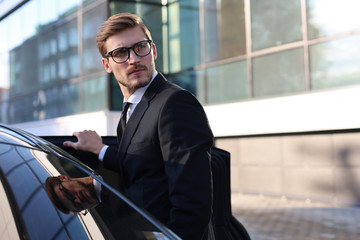 Elegant young businessman entering his car while standing outdoors.