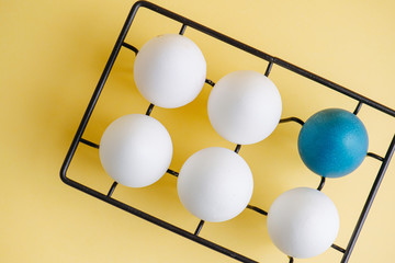 TOp view of one blue egg and five regular ones on a metal egg holder over yellow