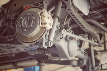 Fototapeta premium car brake part at garage,car brake disc without wheels.Disk brake and car disk brake system service concept - Car disk brake pad replacement service by hand of mechanic man in car garage.Close up.