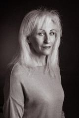 Classic black-and-white dramatic portrait of elderly blonde woman in Studio on black background