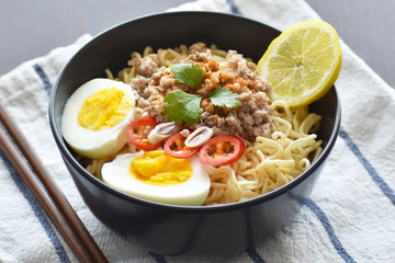 Instant noodles with minced pork, egg, lemon grass, chilli and lemon in a black bowl. Selective focus. Thai style Tom Yum noodles. 
