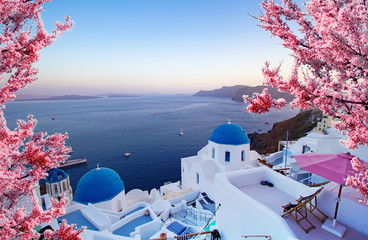 Beautiful view of Oia, Santorini, Greece with pink blossoms flowers at beautiful spring sunset. Vintage colored picture. Business, Love and travel concept - obrazy, fototapety, plakaty