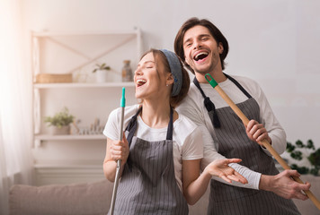 Cheerful Couple Using Mop Handles As Microphones, Having Fun During Spring-Cleaning - obrazy, fototapety, plakaty