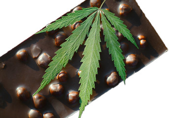 Bar of chocolate with whole nuts containing CBD with green leaf of cannabis on white isolated...