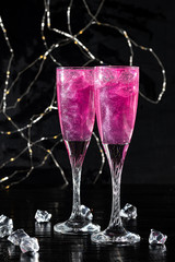 Sparkling brilliant raspberry drink. Champagne in two glasses stands on a wooden table with ice....