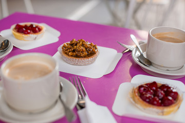 A coffee break with two cups of cappuccino and a purple table with walnut tartlet