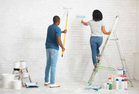 Girl on stepladder and guy paints wall with roller