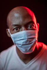 Coronavirus, scared African American man with protective mask, looking at the camera. COVID-19 concept. Studio shot with red light on dark background. Selective focus.