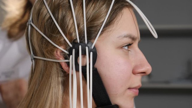 Doctor connecting electronic sensors with wires to female patient. Young woman wired to EEG machine or electroencephalograph which produces graphical record of brain electrical activity