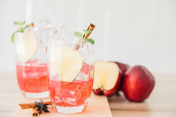 Delicious red apple fruit cocktail iced beverage with cinnamon herb and anise on wooden table. Copy space for your text.