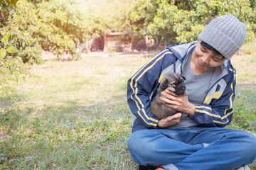 Smile Asian owner carrying, hugging adorable puppy dog on her sitting green grass backyard lawn