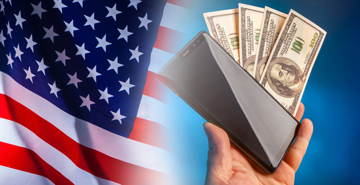 Payment for mobile communications in the United States. Mobile phone contract. Using a mobile Internet Bank. Smartphone and dollars in the hands of the user on the background of the flag of America. - Powered by Adobe