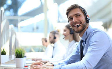 Portrait of call center worker accompanied by his team. Smiling customer support operator at work. - obrazy, fototapety, plakaty