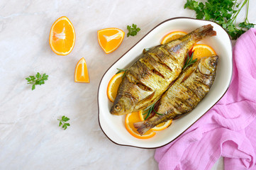 Baked roach fish with vegetables and oranges in a ceramic bowl. Top view. Diet menu.