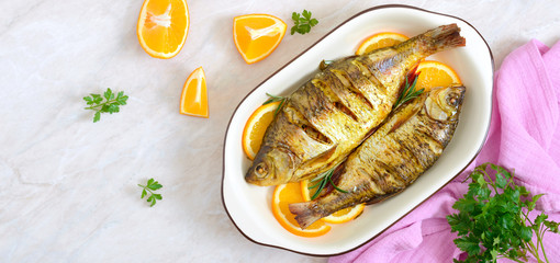 Baked roach fish with vegetables and oranges in a ceramic bowl. Top view. Diet menu. Banner