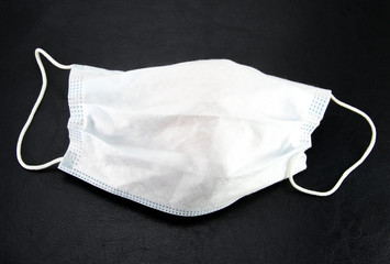 White, thin medical mask with folds on a black textured background. Protection against infections, flu and coronavirus.